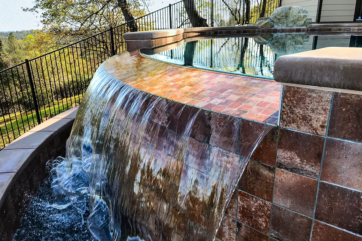 Vanishing edge pool in Colfax featuring a curved catch basin spillway with cascading water and tile detailing.