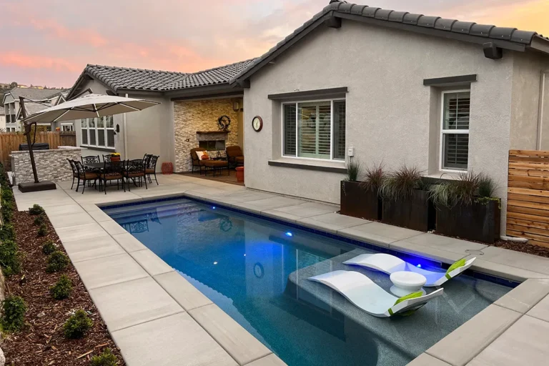 Custom backyard pool designed and built in a small yard with only 5 feet of access, featuring modern in-pool loungers and stone-accented outdoor living.