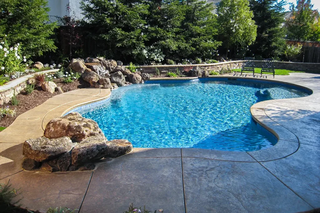 Custom family pool with curved stamped concrete deck and natural stone landscaping
