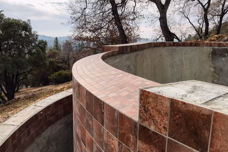 Tile installation along the curved vanishing edge weir wall during construction of a custom hillside gunite pool in Colfax, California.