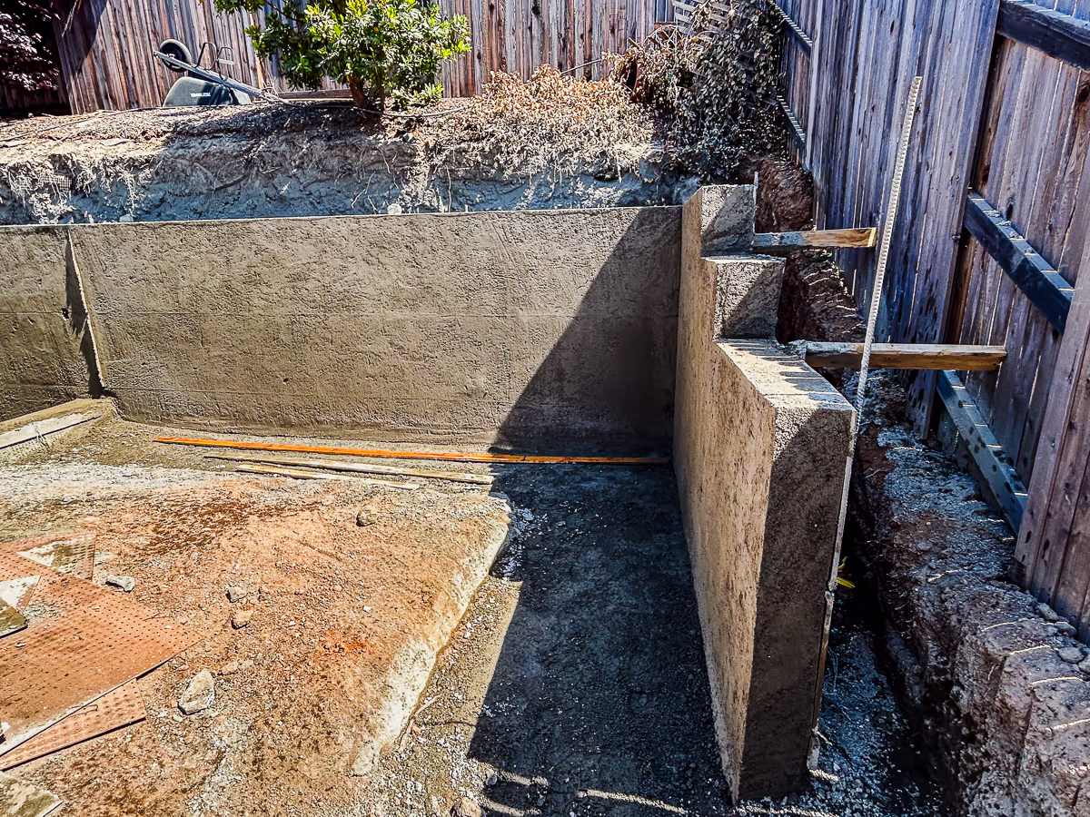 Gunite retaining wall meeting adjacent retaining wall with engineered bond break during small yard pool construction in Rocklin CA