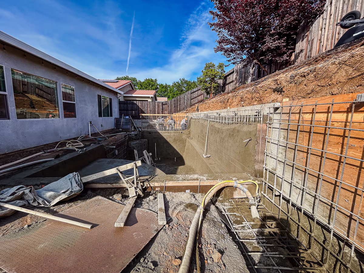 Partially completed gunite pool shell with retaining wall rebar awaiting application on small yard hillside site in Rocklin CA