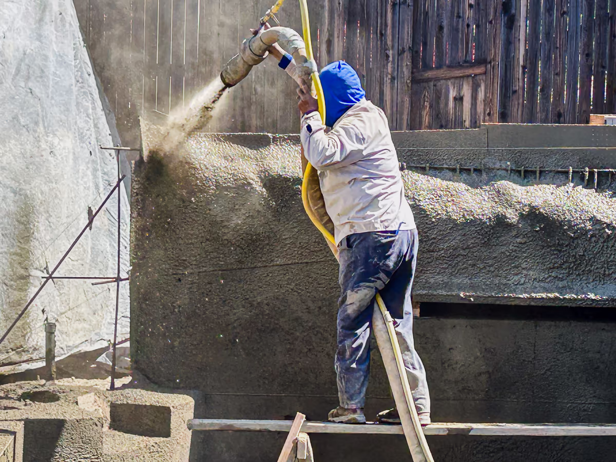 Gunite nozzleman applying gunite to structural retaining wall during small yard pool construction in Rocklin CA