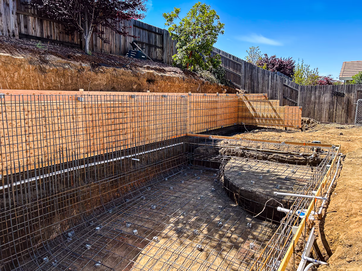 Pool shell rebar grid and plumbing rough-in with retaining wall forms in Rocklin CA backyard