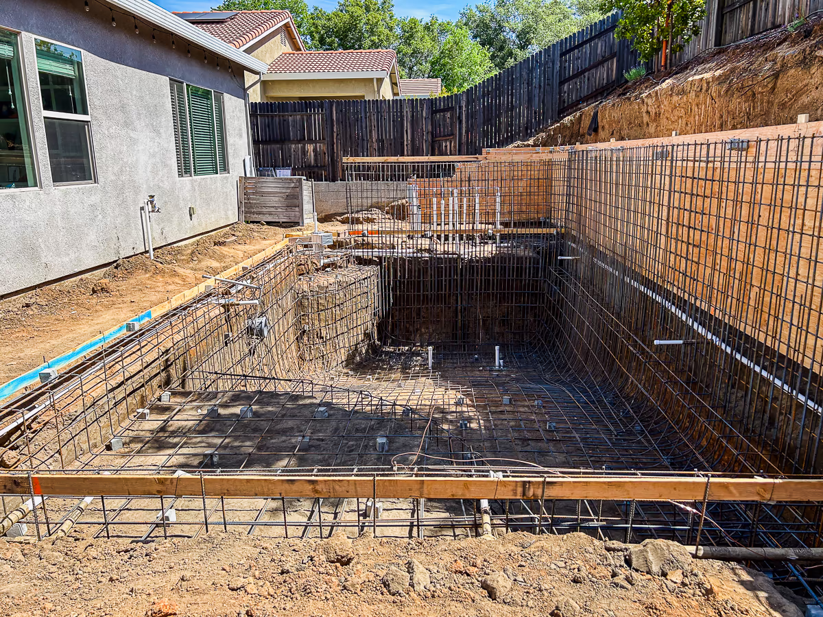 Structural retaining wall rebar and plumbing rough-in against plywood forms before gunite for small yard pool in Rocklin CA