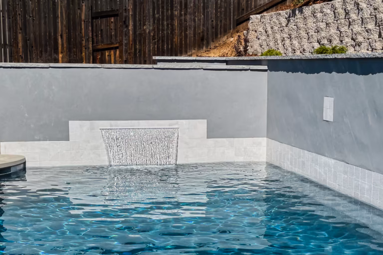 48-inch CMP Classic Falls sheer descent waterfall flowing into Tahoe Blue plaster pool with Slate White tile and Shark Gray retaining wall in Rocklin California