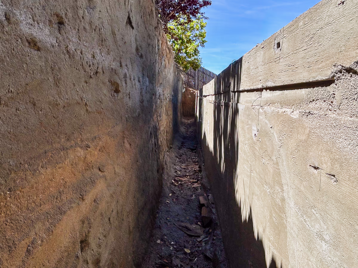 Narrow corridor behind five-foot structural gunite retaining wall at small yard pool construction in Rocklin California