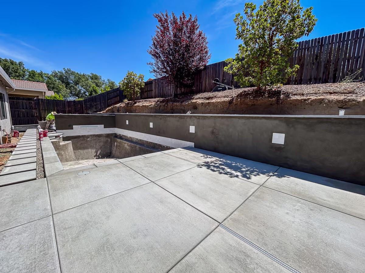 Finished concrete deck with control joints and stucco brown coat applied to the gunite retaining wall at a small yard pool project in Rocklin California