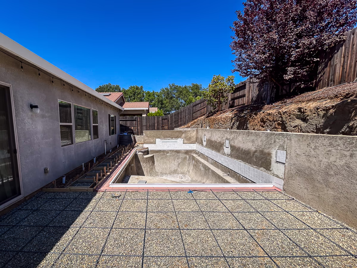 Rebar grid and compacted gravel base prepared for concrete deck pour at small yard hillside pool construction in Rocklin California