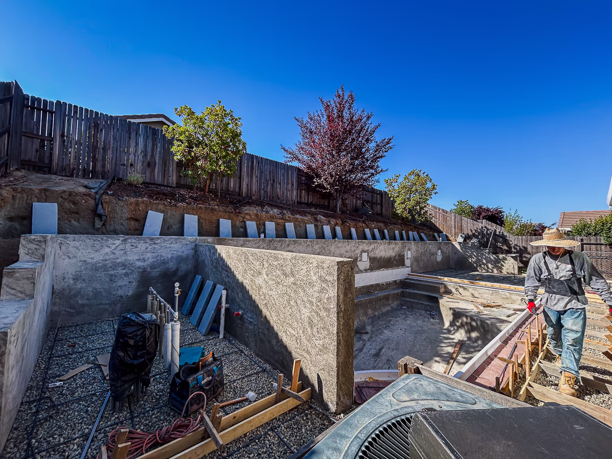 Eldorado Stone Blue Steel wall cap stones being installed on five-foot gunite retaining wall at small yard pool construction in Rocklin California
