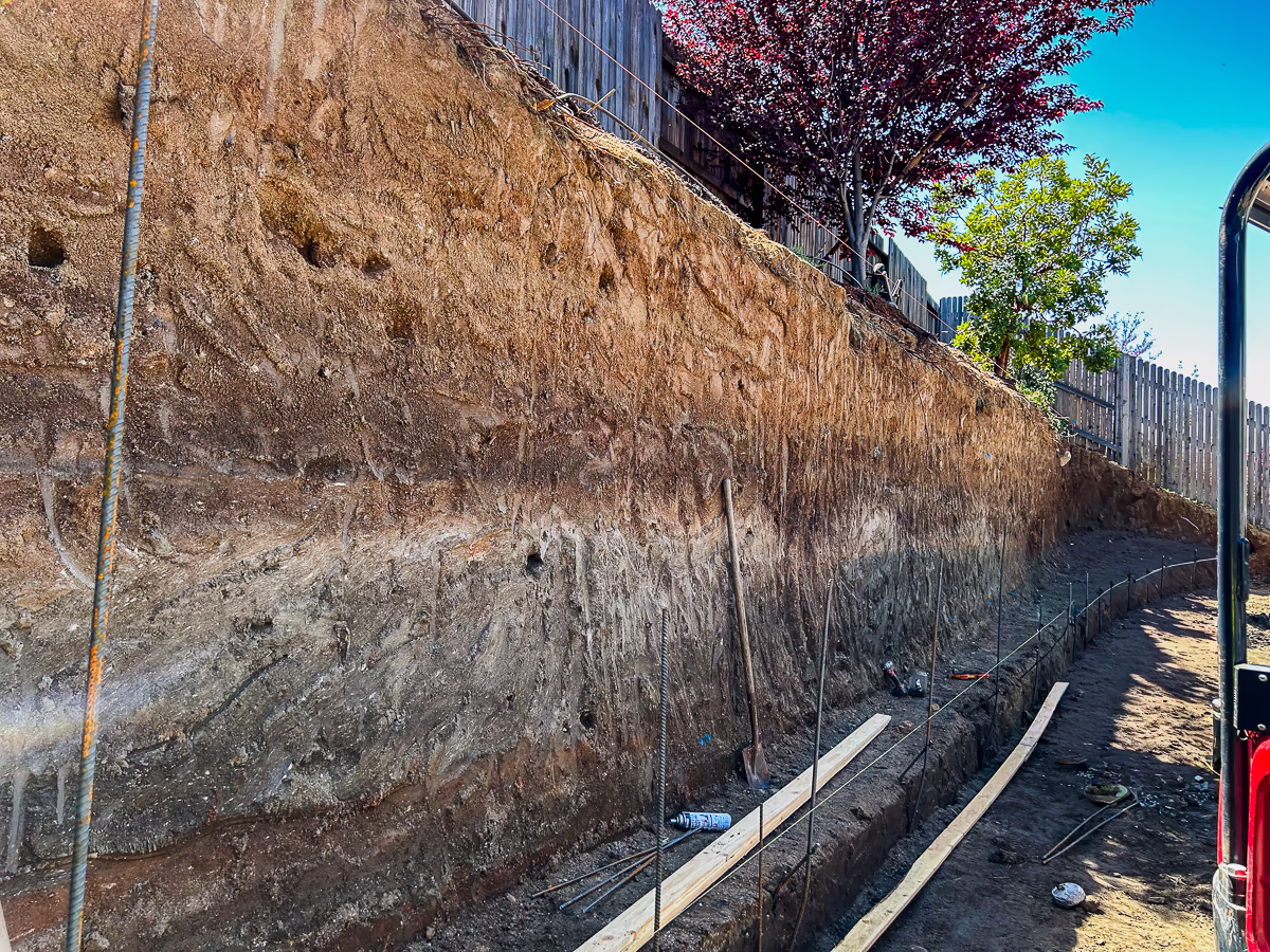 Retaining wall footing trench with rebar dowels and form boards before pool excavation in Rocklin CA