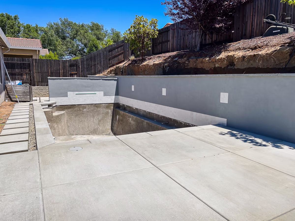 Completed Omega Smooth Coat Acrylic in Shark Gray on gunite retaining wall with Eldorado Stone Blue Steel wall cap and Slate White waterline tile at small yard pool in Rocklin California