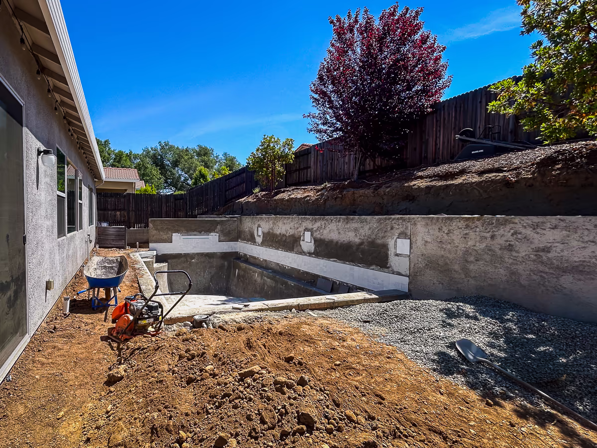 Slate White decorative tile installed on gunite retaining wall with drain gravel and backfill work in progress at small yard pool construction in Rocklin California