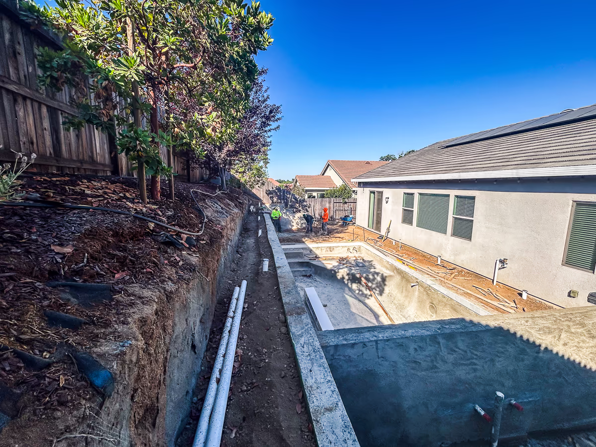 Dual drainage systems installed behind retaining wall at Rocklin hillside pool project including perforated French drain at wall base and separate solid 3-inch surface drain line on hillside