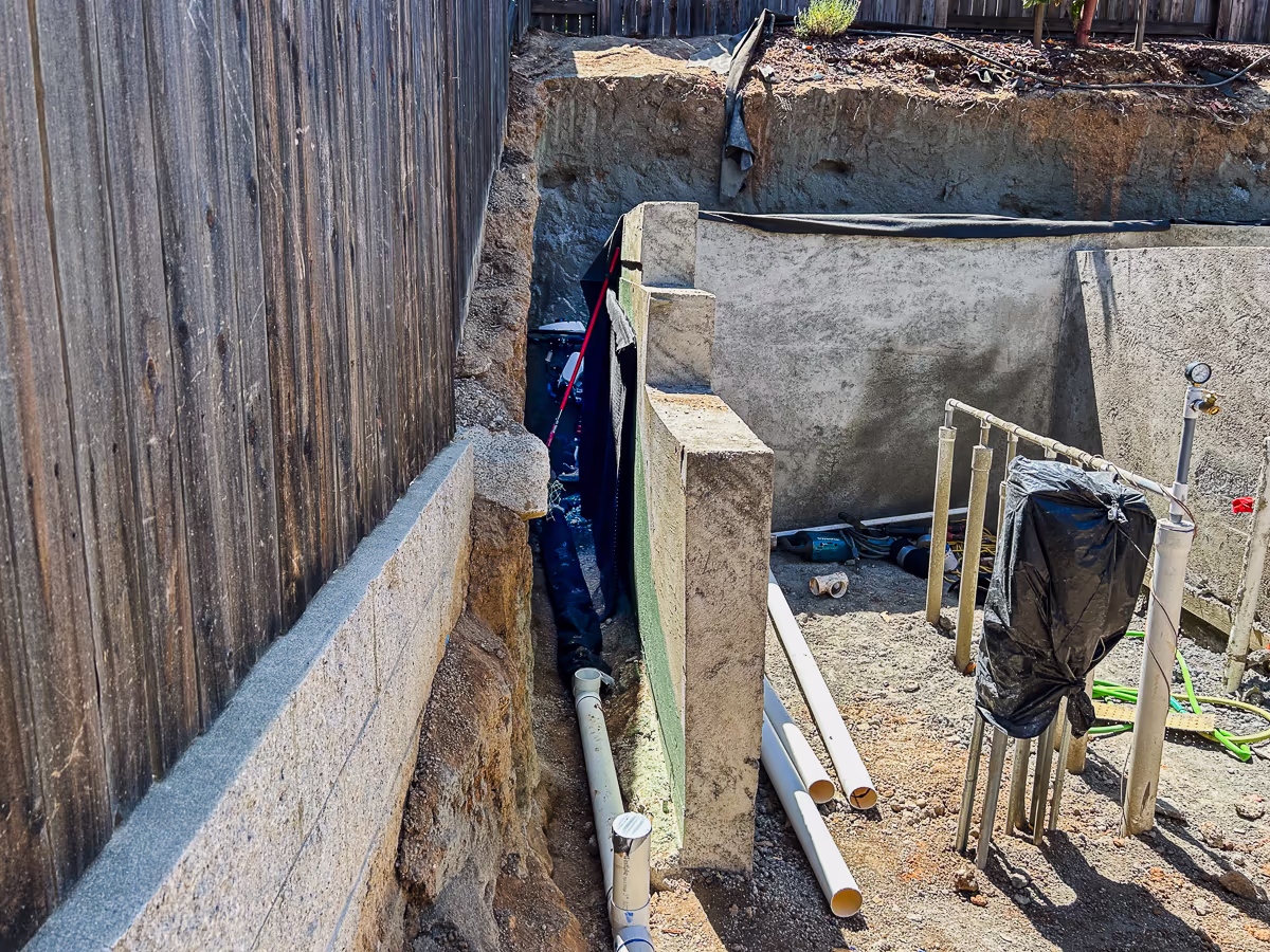 Waterproofing coating, composite sheet drain, and geofabric-wrapped perforated drain line installed behind gunite retaining wall at custom pool construction in Rocklin California
