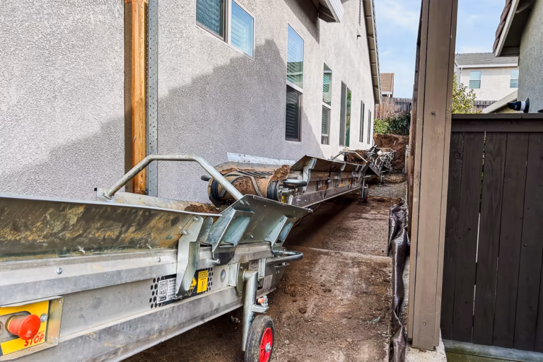 Conveyor belt running through narrow side yard access corridor during pool excavation in Rocklin CA