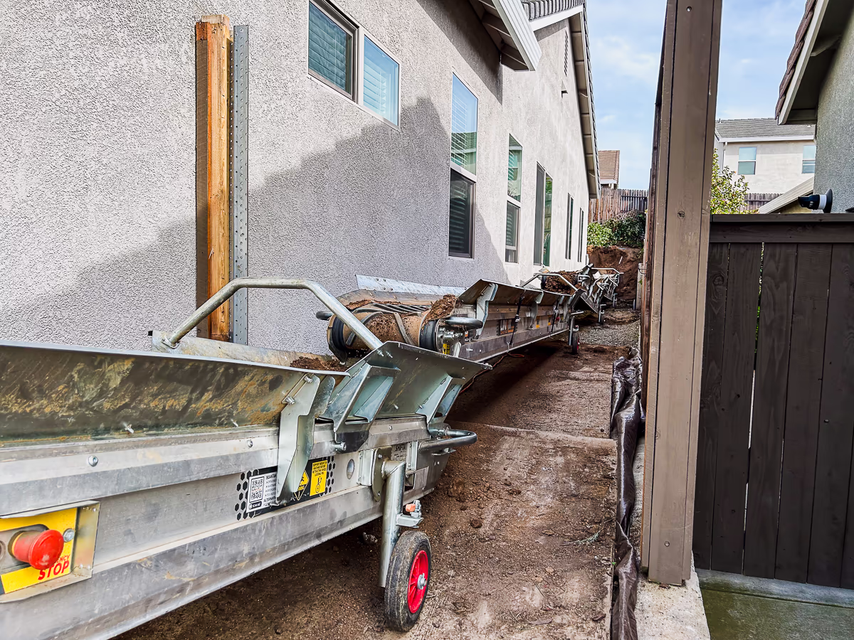 Conveyor belt running through narrow side yard access corridor during pool excavation in Rocklin CA
