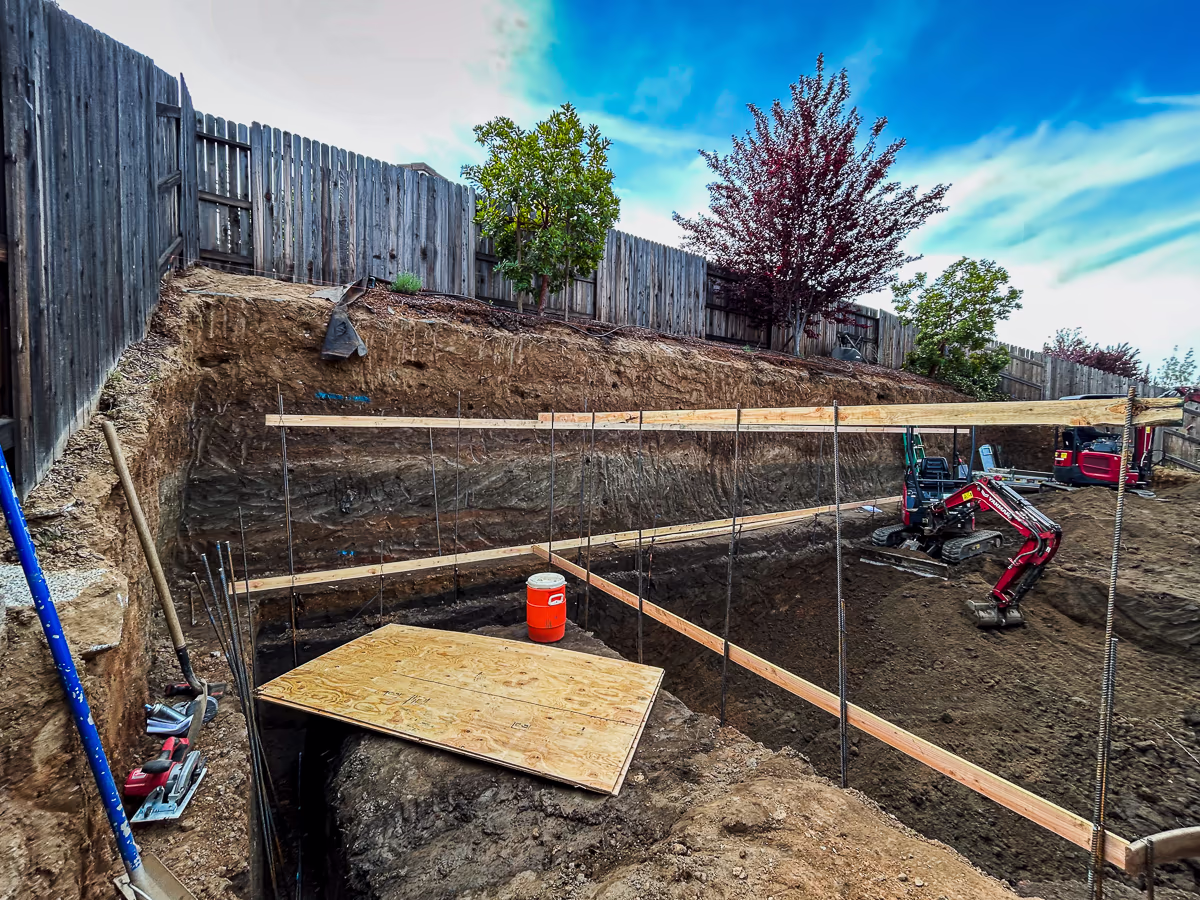 Pool excavation in progress with rebar dowels and form boards in small backyard in Rocklin CA