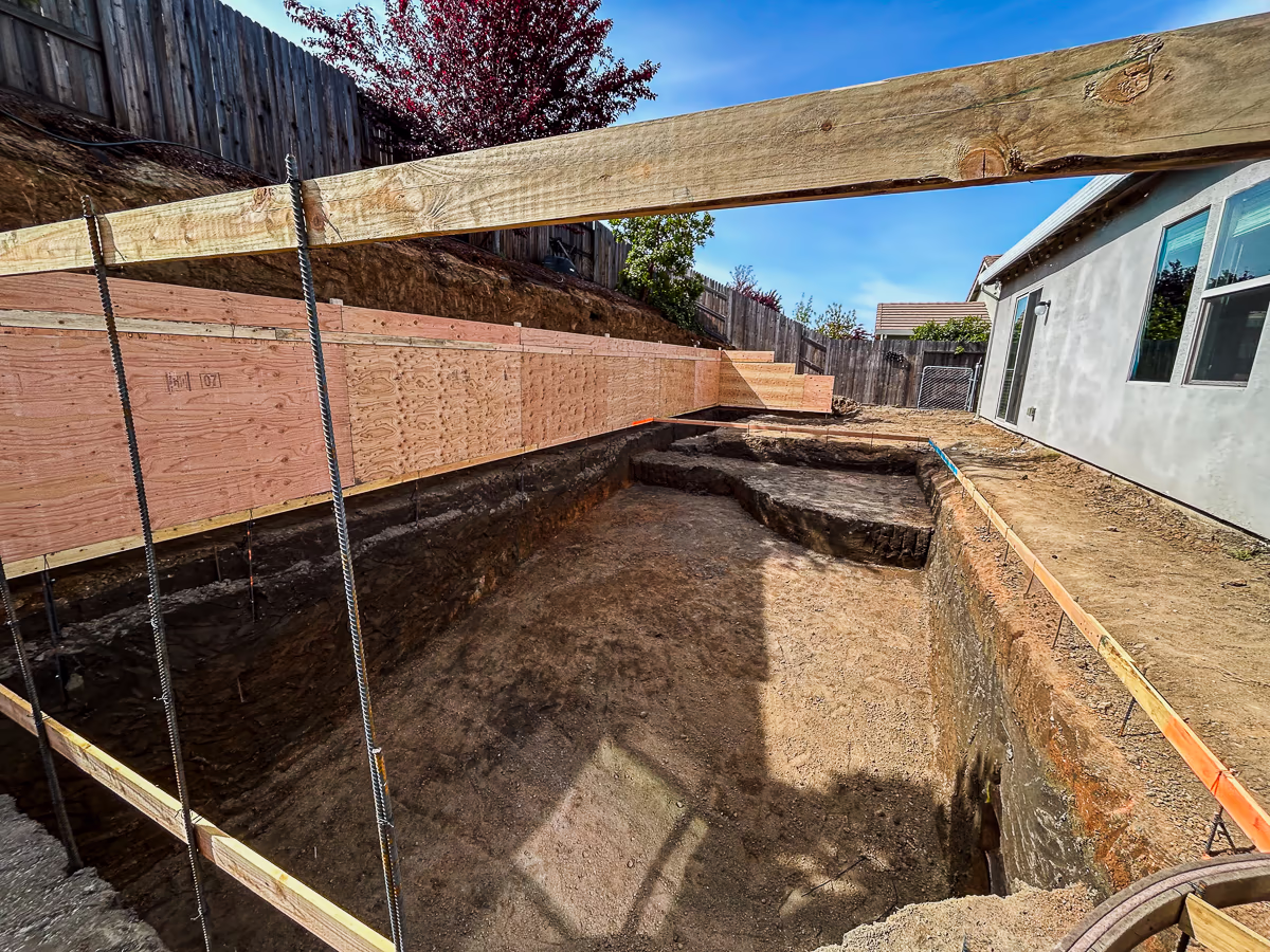 Finished pool excavation with retaining wall form boards placed along slope in Rocklin CA backyard