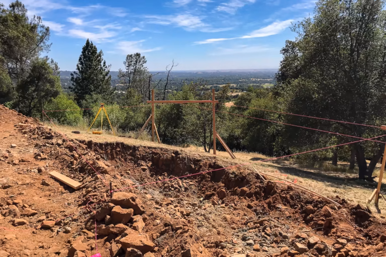 Survey instrument and batter boards establishing pool layout during Auburn hillside vanishing edge pool excavation — Jim Chandler Pools