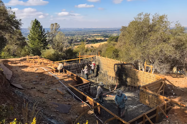 Gunite crew placing shotcrete on the Auburn hillside vanishing edge pool shell with Sacramento Valley panorama behind — Jim Chandler Pools