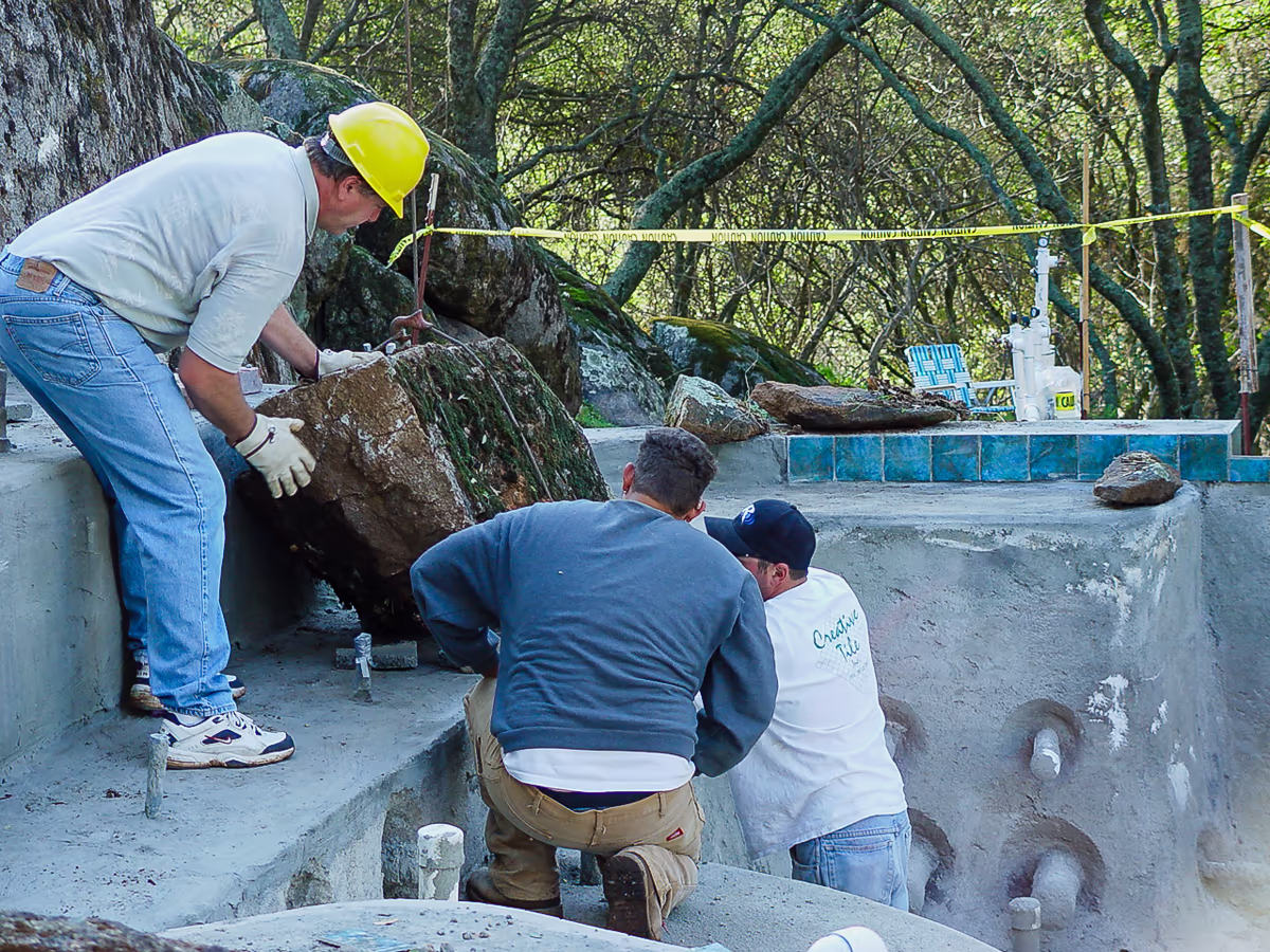 Crew hand-placing native granite waterfall boulder during river pool construction in Sierra foothills of Placer County by Jim Chandler Pools